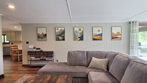 A living room with a sectional sofa, a coffee table, and a bookshelf. - Cabin with Private Pond - 61 Acres - Close to Gore (Johnsburg)
