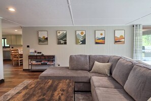 A living room with a sectional sofa, a coffee table, and a bookshelf. - Cabin with Private Pond - 61 Acres - Close to Gore (Johnsburg)