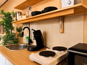 A kitchen with a stainless steel sink, a kettle, a coffee maker, and a microwave. There are wooden shelves above the counter holding plates and a bottle. - Quiet & Cozy Studio Near the Heath (Schneverdingen)