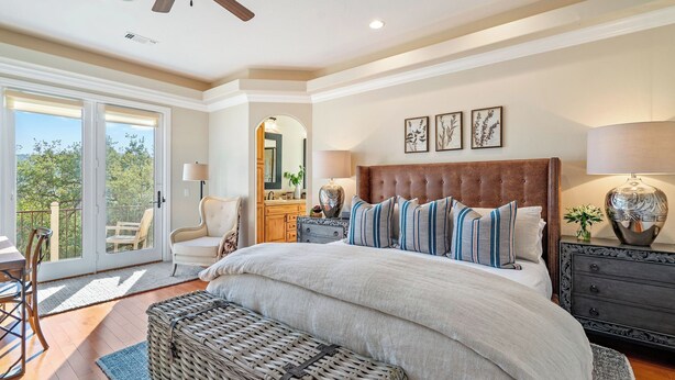 Un dormitorio con una cama grande, una silla, un aparador y vistas al exterior.