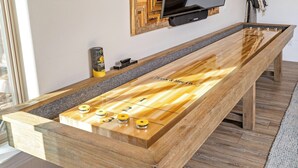 Una mesa de futbolín de madera con superficie lisa y fichas numeradas, ubicada en una habitación con un televisor montado en la pared.