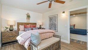Un dormitorio con cama, mesitas de noche, ventilador de techo, planta en la pared y una obra de arte enmarcada.