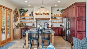 A spacious kitchen with wooden cabinets, a central island with bar stools, and a hanging light fixture. - Hilltop Hacienda by Avantstay Game Room + Hot Tub Hilltop Paso Views (Paso Robles)