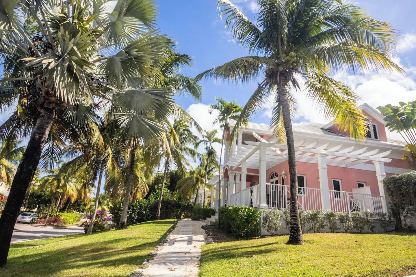 A pathway leading to a pink building with a white porch, surrounded by palm trees.