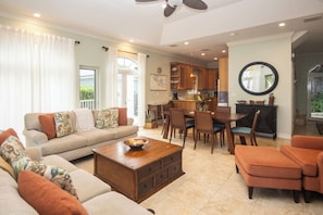 A living room with a sofa, ottoman, coffee table, and a dining area with chairs and a table. - Paradise Villa - 3BR / 3BA w/ Boat Slip in February Point (George Town)
