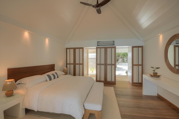 A bedroom with a bed, bedside tables, a ceiling fan, and a view of the outdoors.