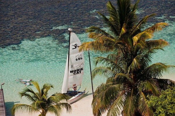 A sailboat with the number 680 on its sail, docked near a beach with clear turquoise water and palm trees.