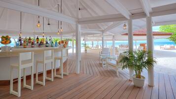 A covered outdoor bar area with a wooden floor, white bar stools, and a variety of bottles.