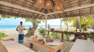 A beachside gazebo with a wooden table, chairs, and hanging lights.