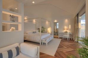 A modern bedroom with a four-poster bed, a sitting area with a chair and a small table, and a desk with a chair. - Diamonds Athuruga Maldives Resort and SPA (Athuruga Island)