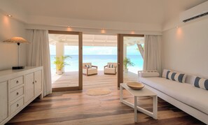 A room with a wooden floor, a sofa, a table, a lamp, and a view of the ocean.