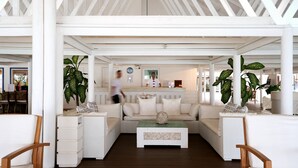 A spacious, white-roofed lounge area with a central seating arrangement, surrounded by large potted plants and wooden chairs. - Diamonds Athuruga Maldives Resort and SPA (Athuruga Island)