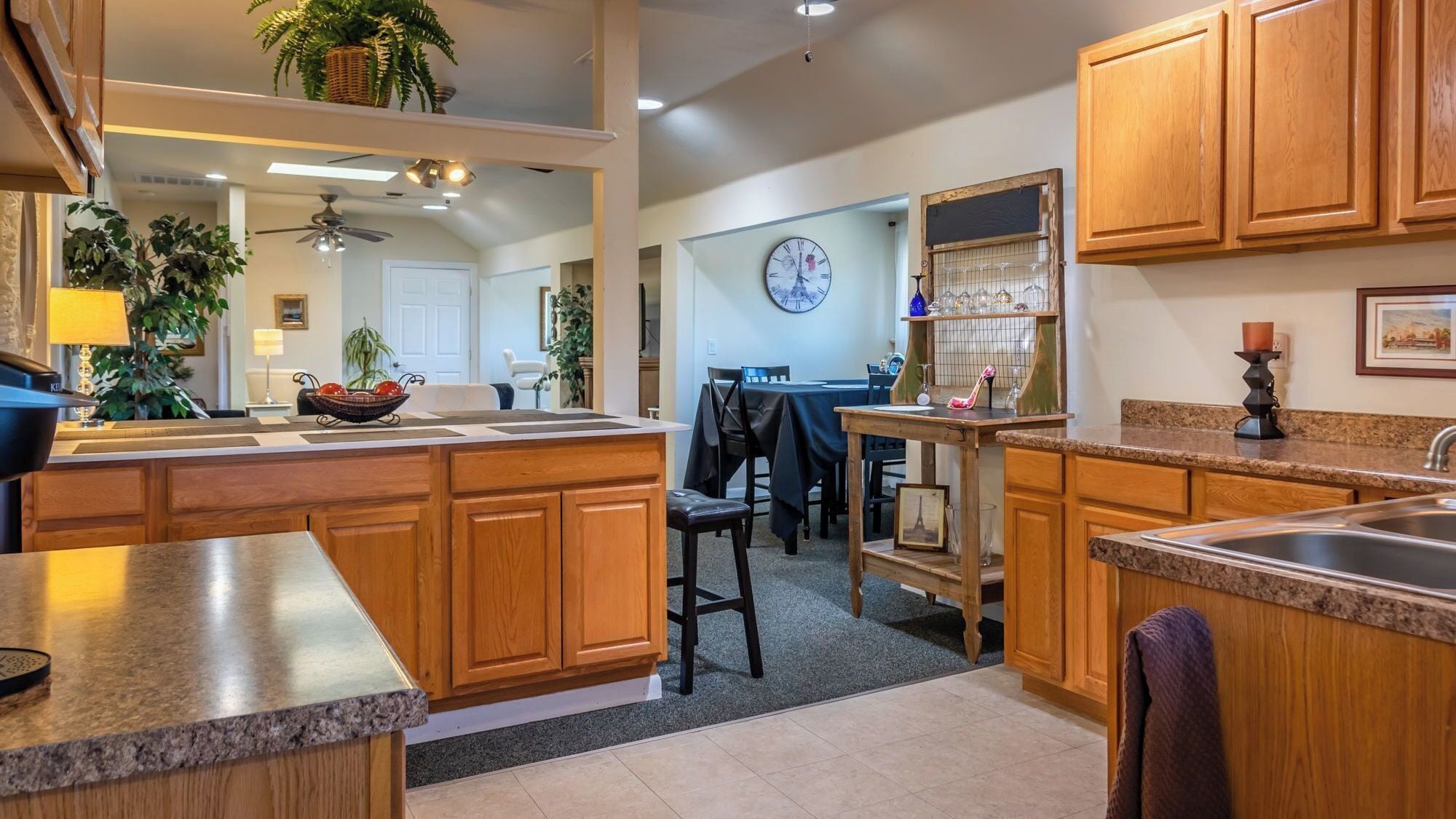 A kitchen with wooden cabinets, a granite countertop, a dining area with a table and chairs, and a clock on the wall.