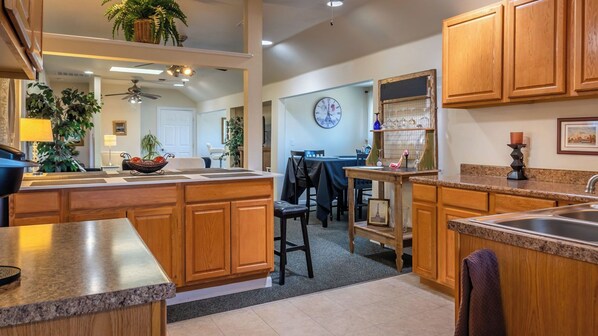 A kitchen with wooden cabinets, a granite countertop, a dining area with a table and chairs, and a clock on the wall.