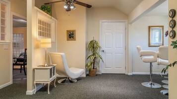 A hallway with a white door, a ceiling fan, a lamp, a chair, a potted plant, and a mirror on the wall.