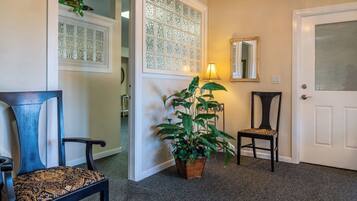 A hallway with a potted plant, two chairs, a door with a mirror, and a window with frosted glass panels.