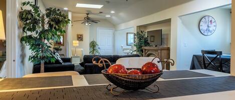 A living room with a dining area, ceiling fans, and a clock on the wall.