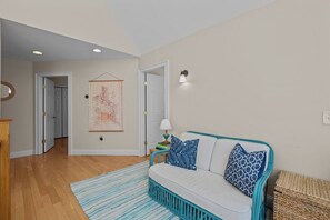Ein Wohnzimmer mit einer Couch, einem Teppich, einer Lampe und einem an der Wand hängenden Kunstwerk.