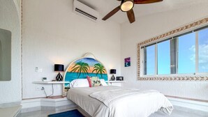 Quarto com cama, ventoinha no teto, janela grande e ar condicionado fixado na parede.