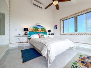 A bedroom with a bed, a ceiling fan, a large window, and a wall-mounted air conditioner. - Penthouse Paradise | Wraparound Ocean Views (Isla Mujeres)