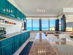 A kitchen with a view of the ocean, featuring teal cabinets, granite countertops, and a dining area with a view. - Penthouse Paradise | Wraparound Ocean Views (Isla Mujeres)