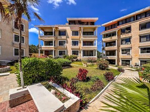 A multi-story hotel with a central courtyard featuring landscaped gardens and palm trees. - Penthouse Paradise | Wraparound Ocean Views (Isla Mujeres)