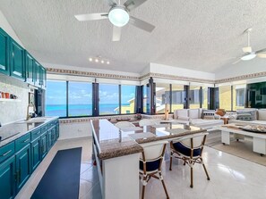 A spacious kitchen with a large island, a dining area with a view, and a ceiling fan. - Penthouse Paradise | Wraparound Ocean Views (Isla Mujeres)