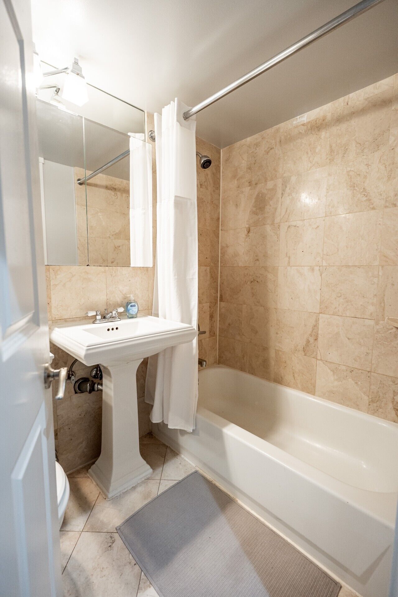 A bathroom with a white sink, a bathtub, and beige tiled walls.