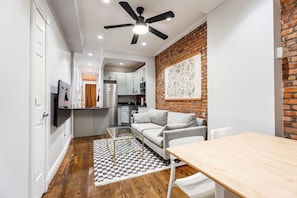 A compact living space with a kitchenette, a sofa, a dining table, and a ceiling fan. - Charming 2BR Garden Apt on Tree-Lined Street (New York)