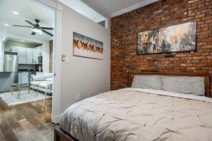 A bedroom with a brick wall, a bed with striped bedding, and a painting above the bed. - Charming 2BR Garden Apt on Tree-Lined Street (New York)