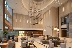 A spacious lobby with a central staircase, seating areas, and a reception desk.