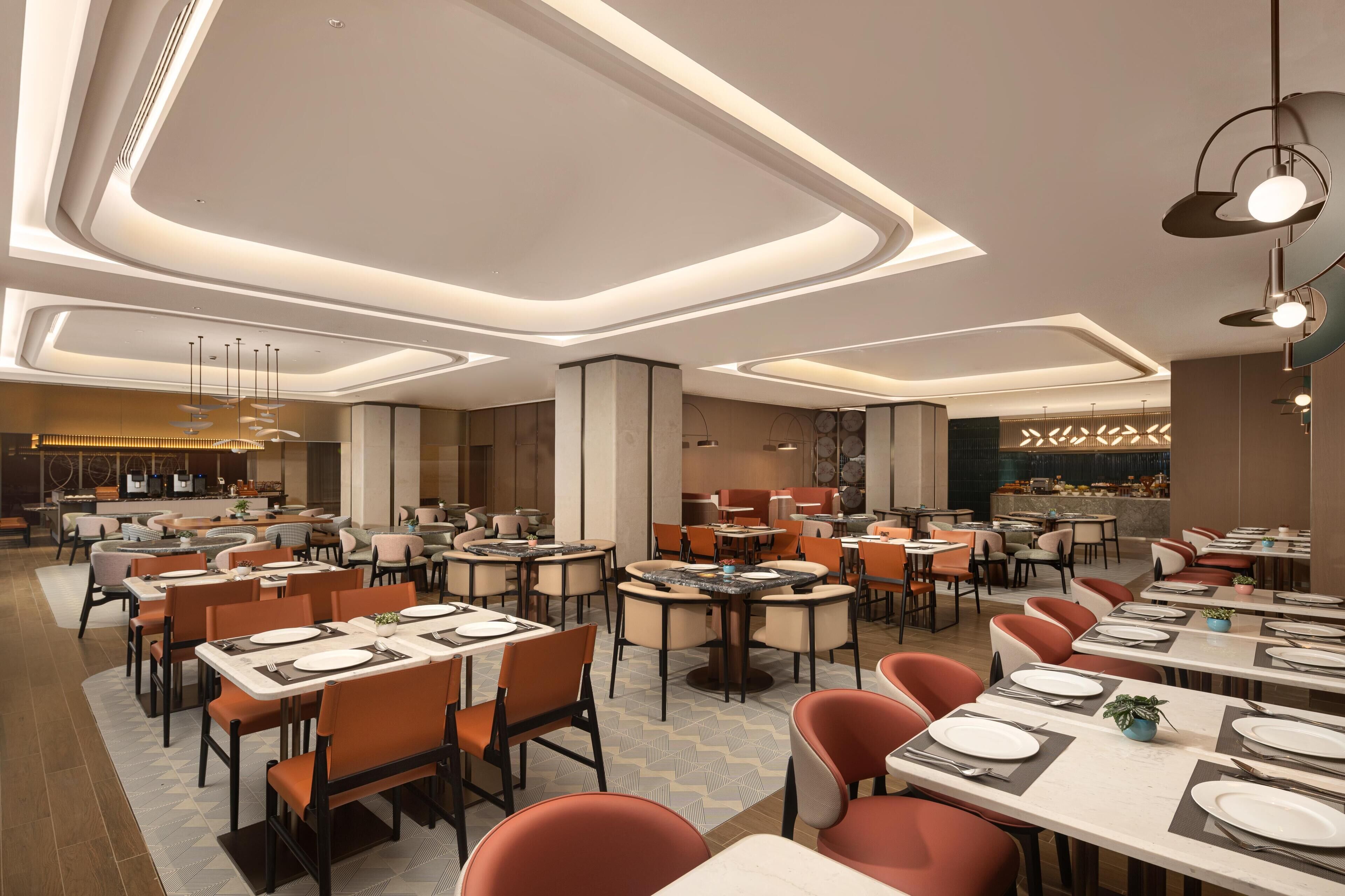 A spacious restaurant with multiple dining areas, modern lighting fixtures, and a variety of seating arrangements.