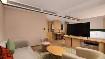 Une chambre d’hôtel moderne équipée d’un canapé, d’une petite table ronde, d’un téléviseur et d’un bureau avec une chaise.