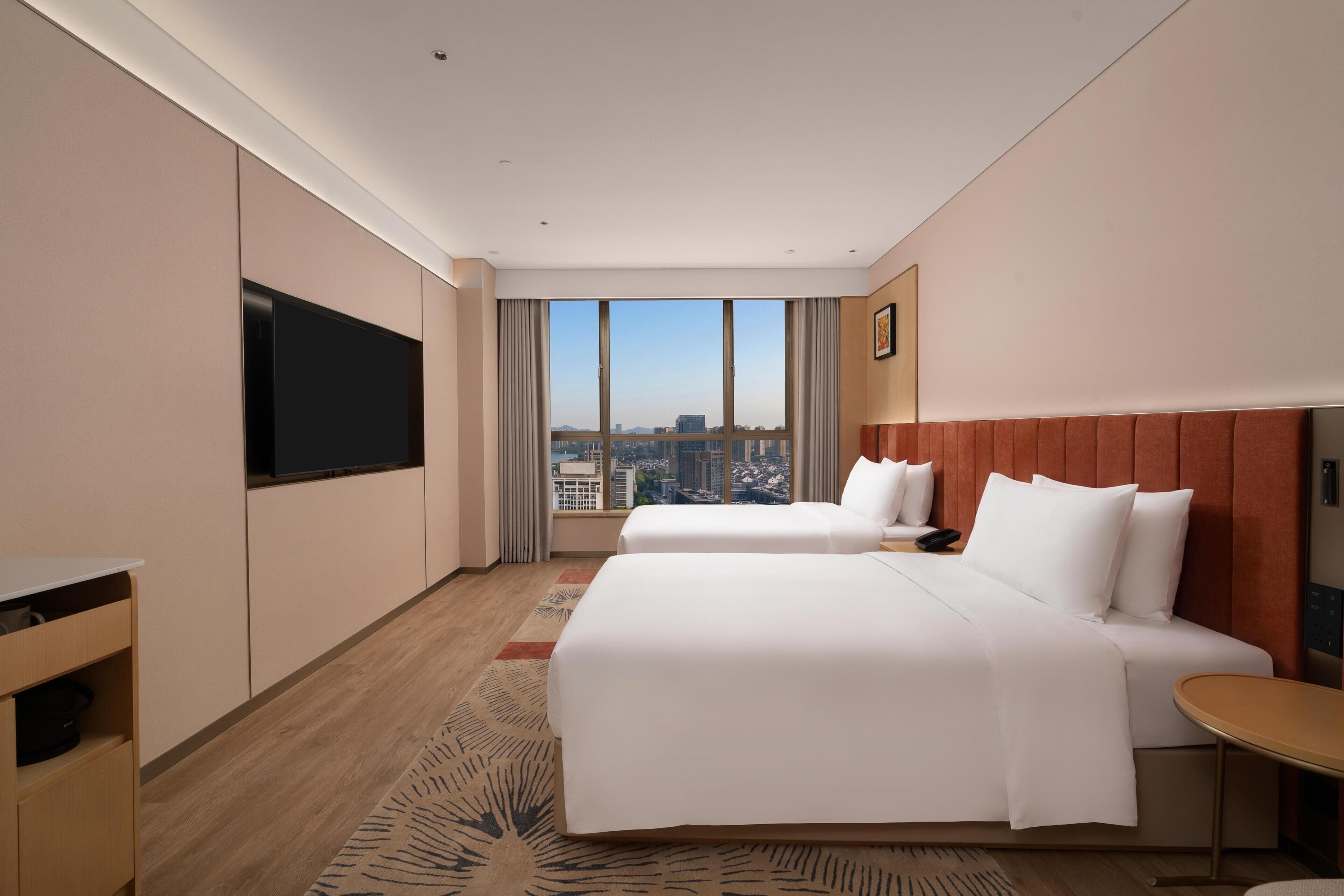 Habitación de hotel con dos camas, televisión, vista a la ciudad y una pequeña mesa.