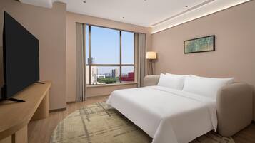 Quarto de hotel com cama, escrivaninha, televisão, janela com cortinas, luminária e vista para a cidade.
