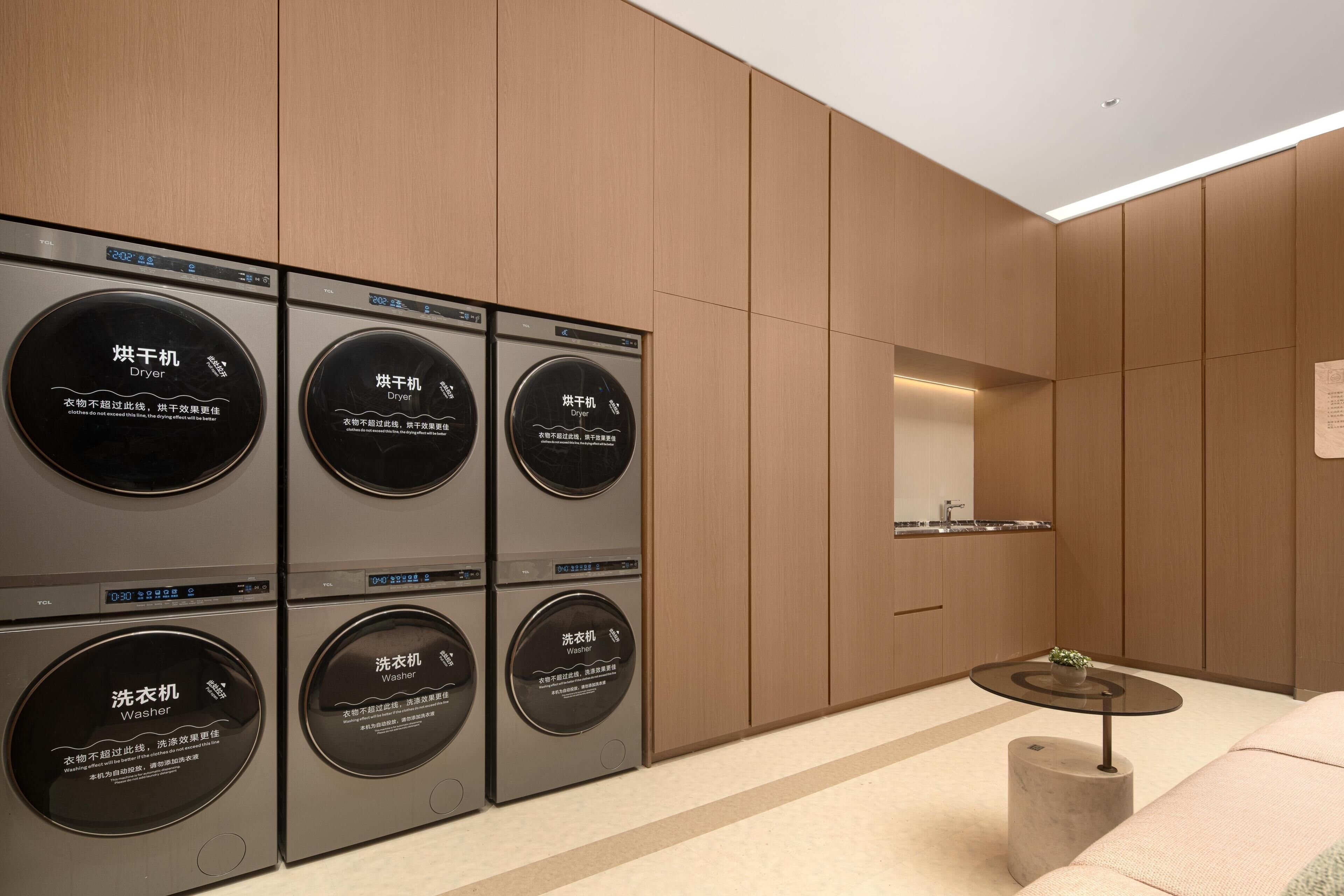 A modern laundry room with six washing machines and dryers, a small table, and a mirror on the wall.