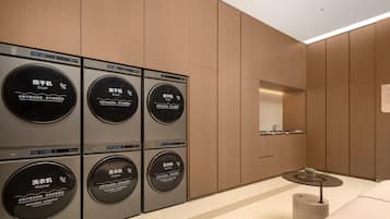 A modern laundry room with six washing machines and dryers, a small table, and a mirror on the wall.