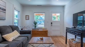 A living room with a grey sofa, a coffee table, a TV stand, and a door leading outside. - Bella Villa - Vine Cottages by Avantstay Hot Tub + Firepit + Bocce Downtown Paso Robles (Paso Robles)