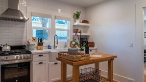 Una cocina moderna con armarios blancos, estufa a gas, campana extractora de acero inoxidable y ventana con vista a árboles.
