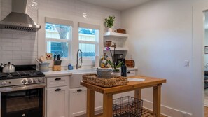 A modern kitchen with white cabinetry, a gas stove, a stainless steel range hood, and a window with a view of trees. - Bella Villa - Vine Cottages by Avantstay Hot Tub + Firepit + Bocce Downtown Paso Robles (Paso Robles)