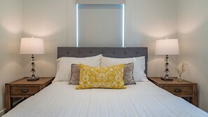 A neatly made bed with a grey headboard, two bedside tables with lamps, and a window above the bed. - Bella Villa - Vine Cottages by Avantstay Hot Tub + Firepit + Bocce Downtown Paso Robles (Paso Robles)