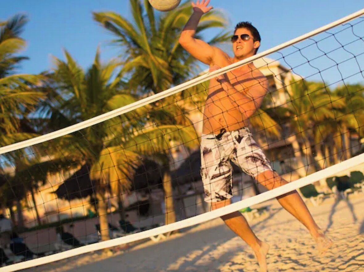 A person playing beach volleyball on a sandy court with palm trees in the background.