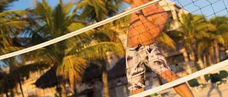 A person playing beach volleyball on a sandy court with palm trees in the background.