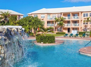A swimming pool with a waterfall feature, surrounded by a building with balconies and palm trees. - Cozy 1-bedroom apartment with AC in welcoming Freeport (Freeport)