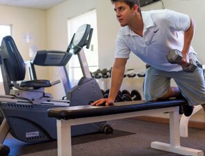 Une salle de sport équipée de matériel d’exercice, notamment un tapis de course et des haltères.