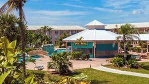 Ein Hotel mit Poolanlage, Palmen und einem Gebäude, an dem ein Schild mit der Aufschrift 'Coconuts' hängt.