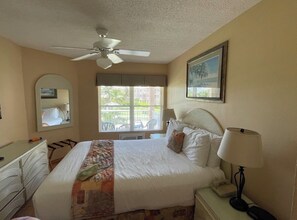 A hotel room with a bed, a ceiling fan, a window with blinds, a bedside table with a lamp, and a dresser. - Cozy 1-bedroom apartment with AC in welcoming Freeport (Freeport)