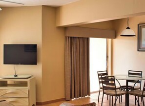 A room with a flat-screen TV on a stand, a dining table with chairs, and a window with curtains. - Cozy 1-bedroom apartment with AC in welcoming Freeport (Freeport)
