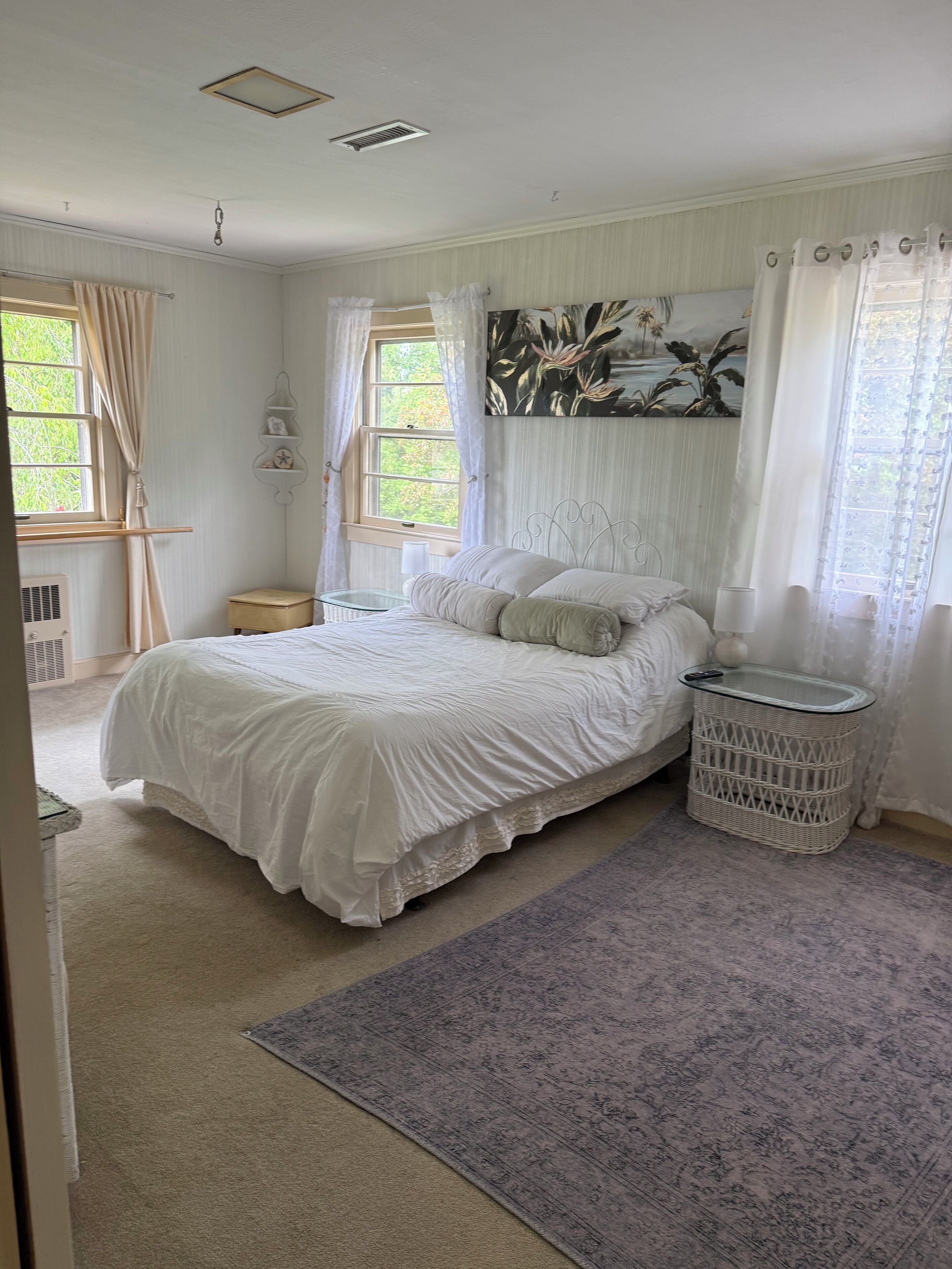 A bedroom with a bed, a nightstand, a lamp, a window with curtains, and a wall-mounted shelf.
