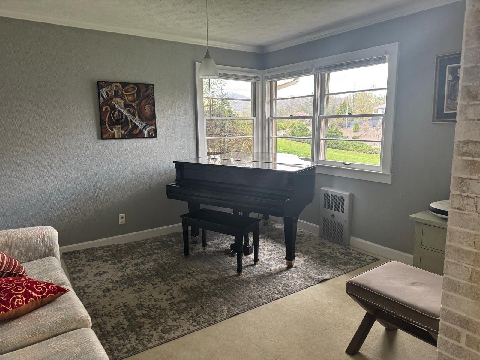 Une pièce comprenant un grand piano, un canapé, un tapis et une fenêtre donnant sur un paysage verdoyant.